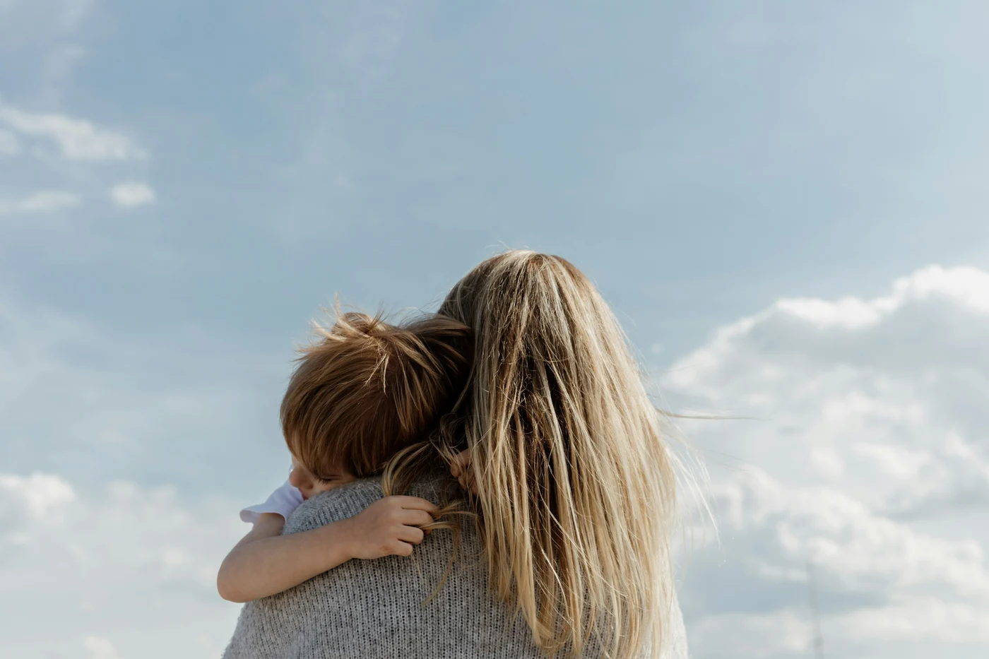 A parent holding a child outdoors beneath an open sky.