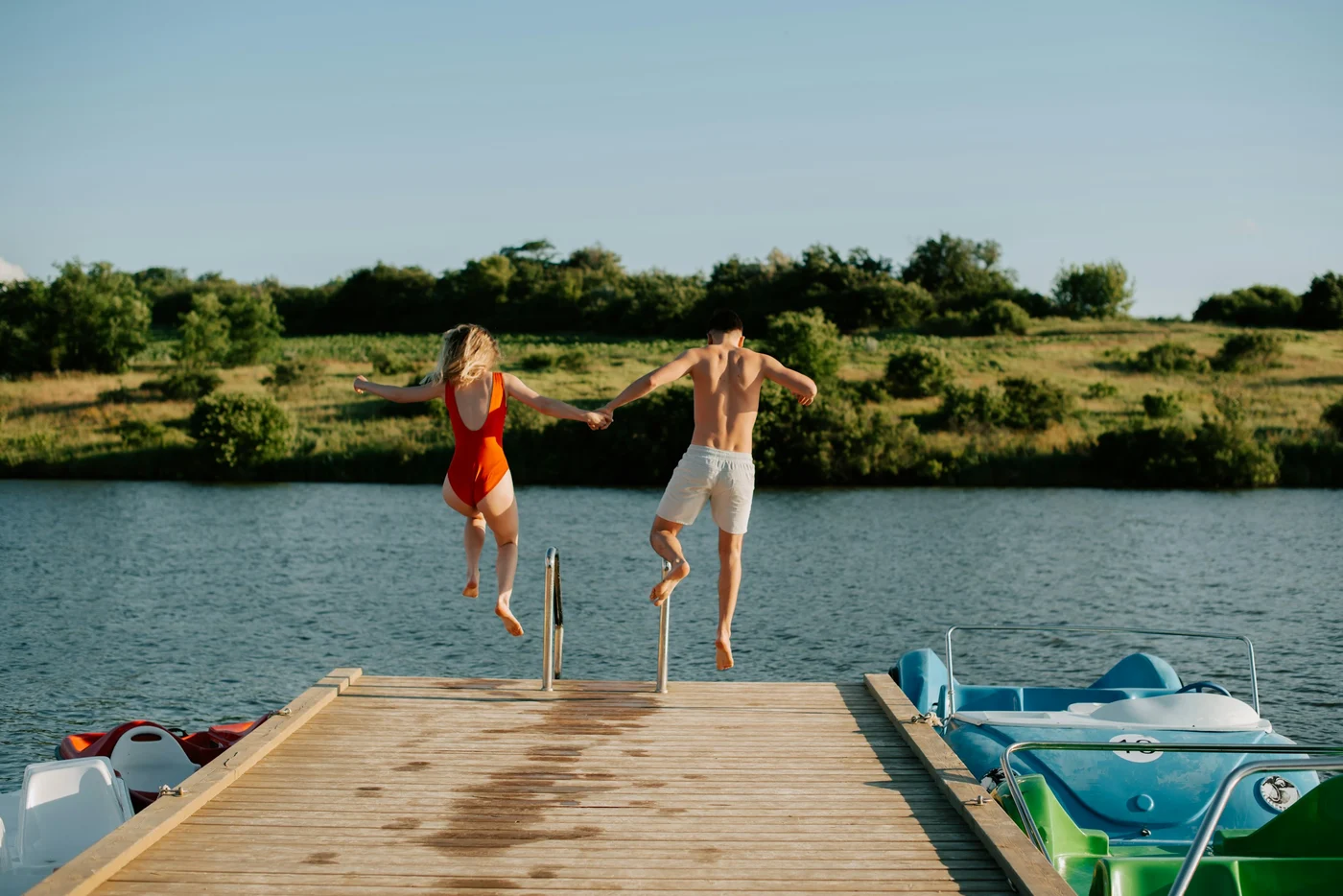 Two people jumping from a wooden dock into a lake.