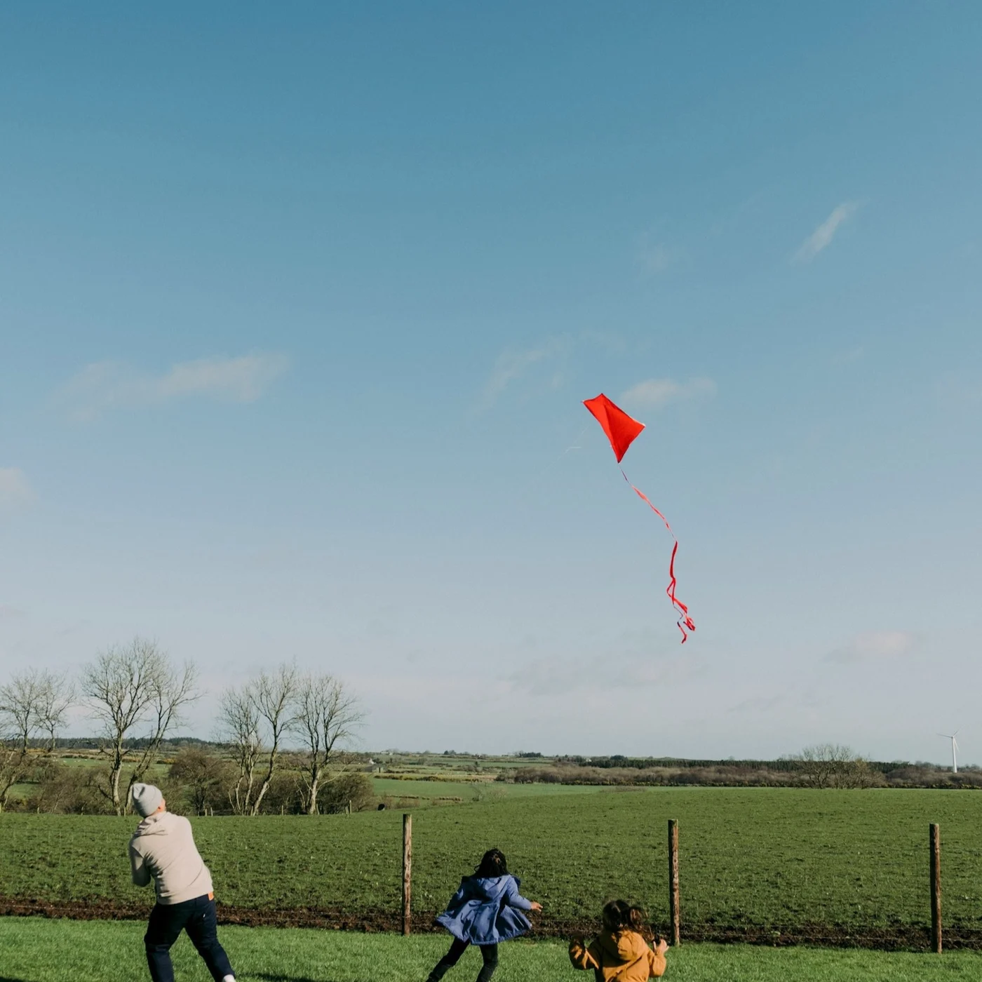 A red kite flying above an open field.